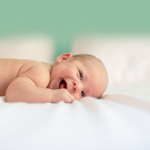 Bébé en train de rire, couché sur le ventre sur une couverture blanche