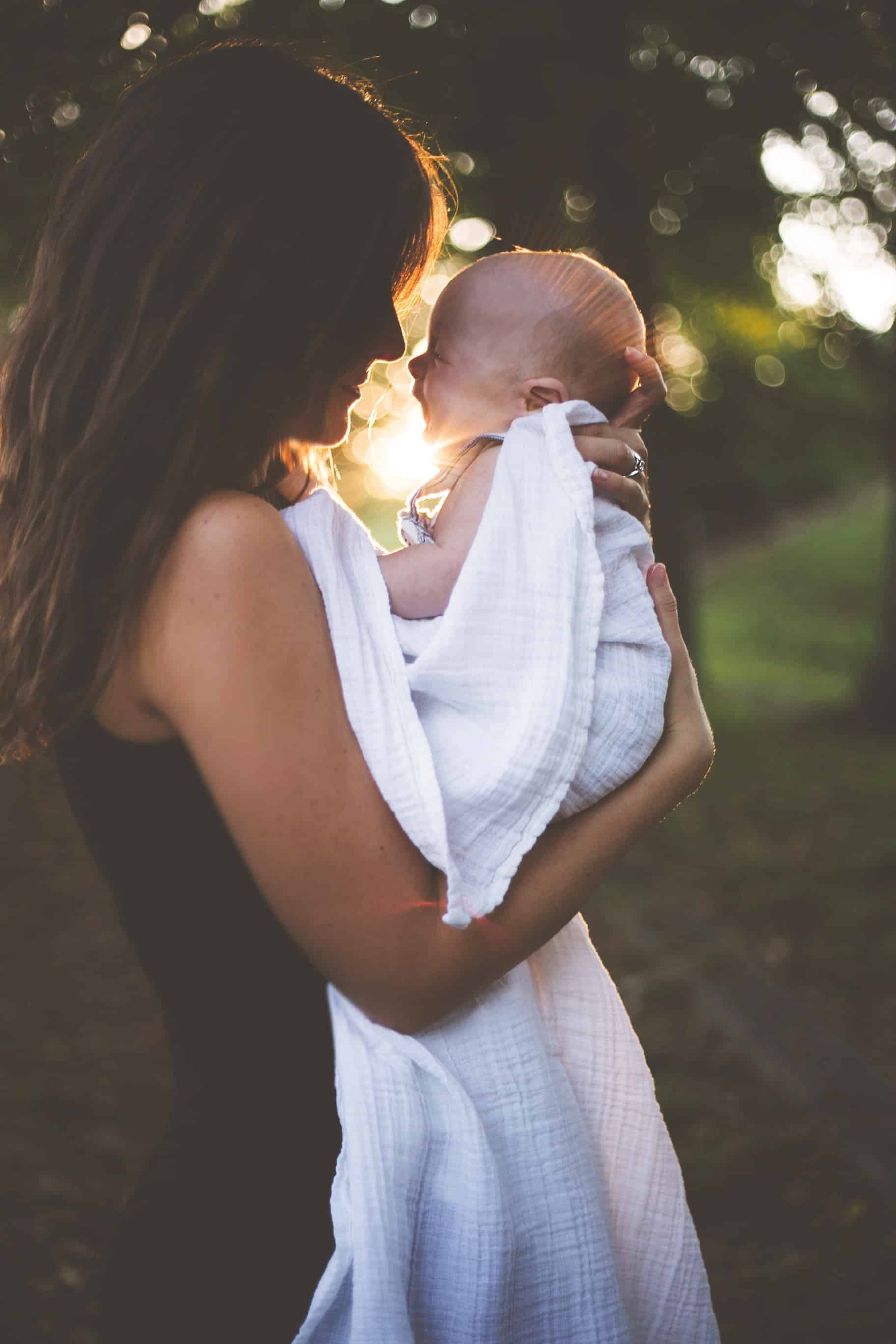 Maman portant son jeune bébé dans les bras avec des arbres en fond